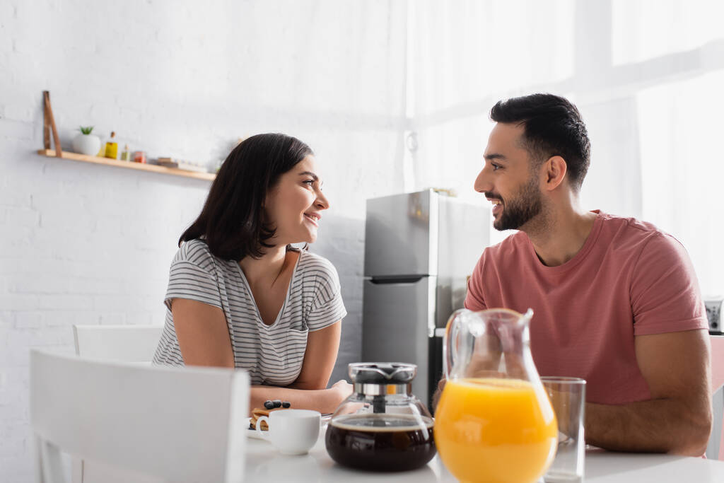 happy young couple sitting at table with breakfast, coffee and orange juice in kitchen - Photo, Image