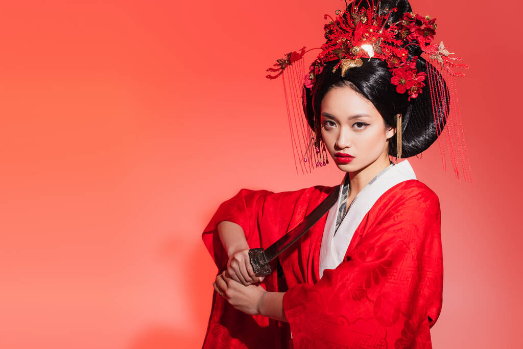 Asiatin mit traditioneller Frisur und Kleidung mit Schwert auf rotem Hintergrund  - Foto, Bild