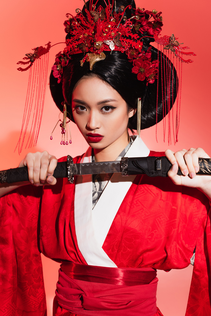 Mujer asiática en kimono tradicional sosteniendo espada sobre fondo rojo  - Foto, Imagen