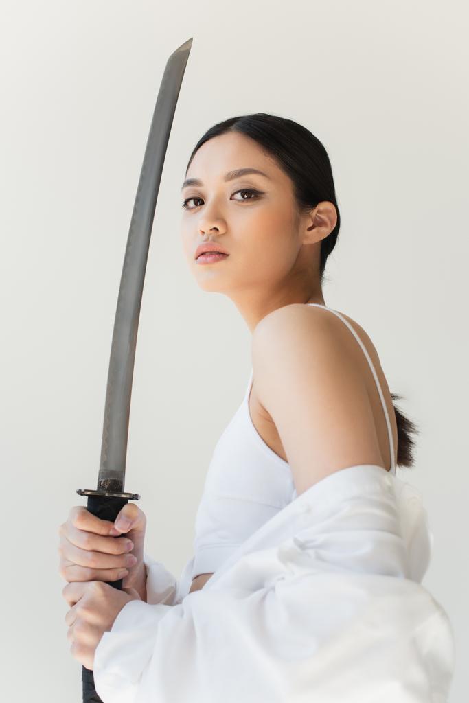 Low angle view of japanese woman with sword looking at camera isolated on grey - Photo, Image