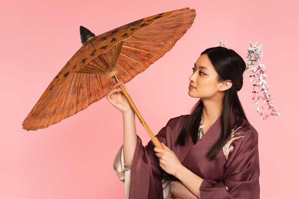 Side view of japanese woman holding traditional umbrella isolated on pink  - Photo, Image
