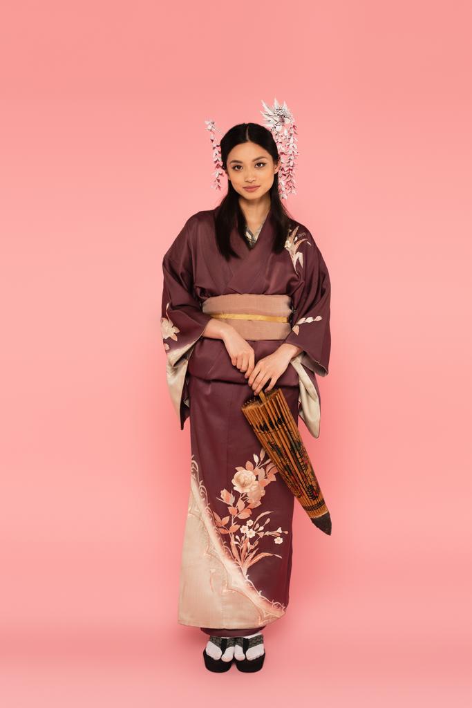 Femme japonaise avec coiffure traditionnelle et parapluie kimono sur fond rose - Photo, image
