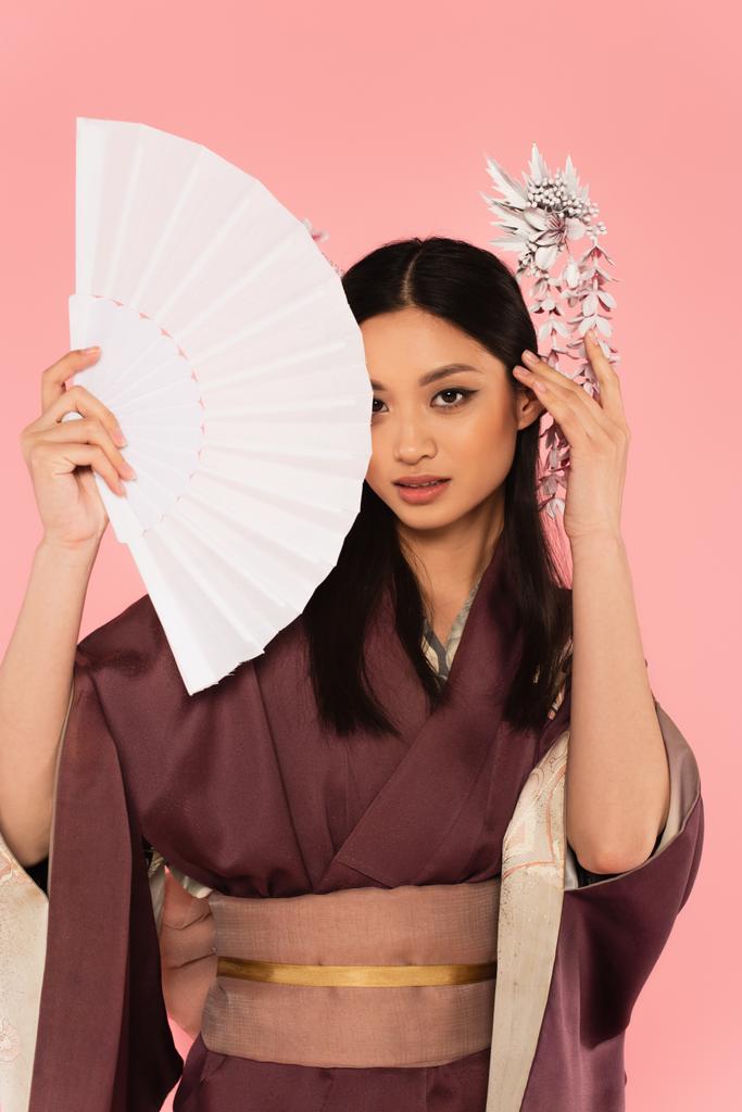 Aziatische vrouw in traditionele kleding houden ventilator geïsoleerd op roze  - Foto, afbeelding