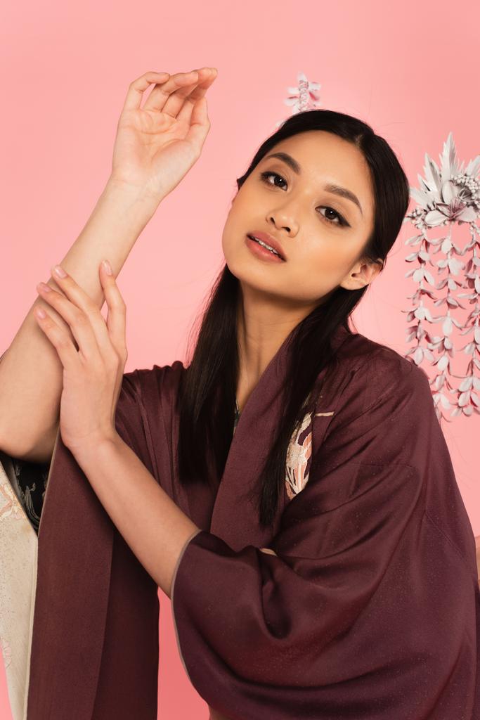 Schön asiatisch frau im kimono posieren und schauen bei camera isolated auf rosa  - Foto, Bild