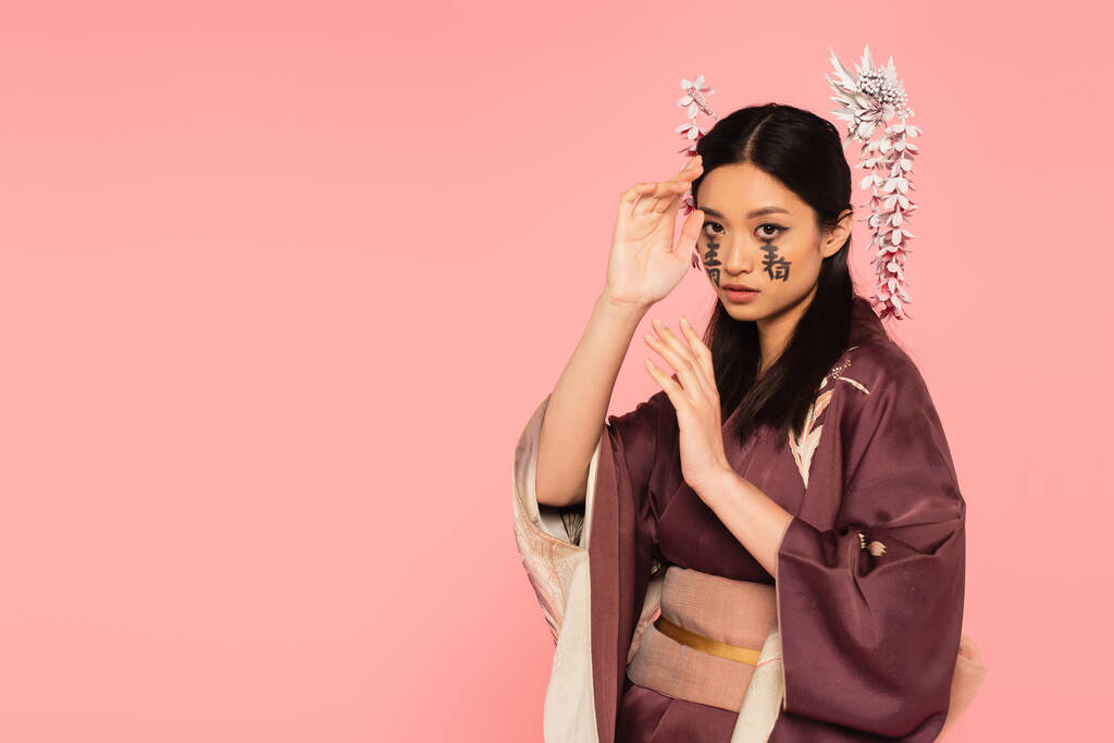 Young asian woman with hieroglyphs on face posing isolated on pink  - Photo, Image