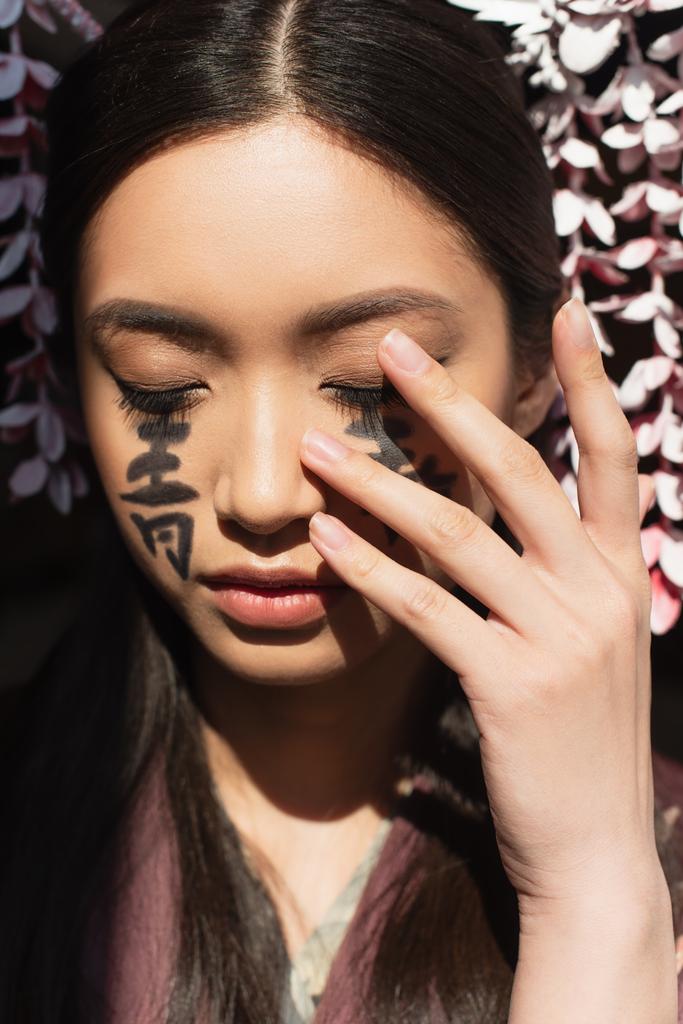 Giapponese donna con geroglifici toccare faccia isolato su nero  - Foto, immagini