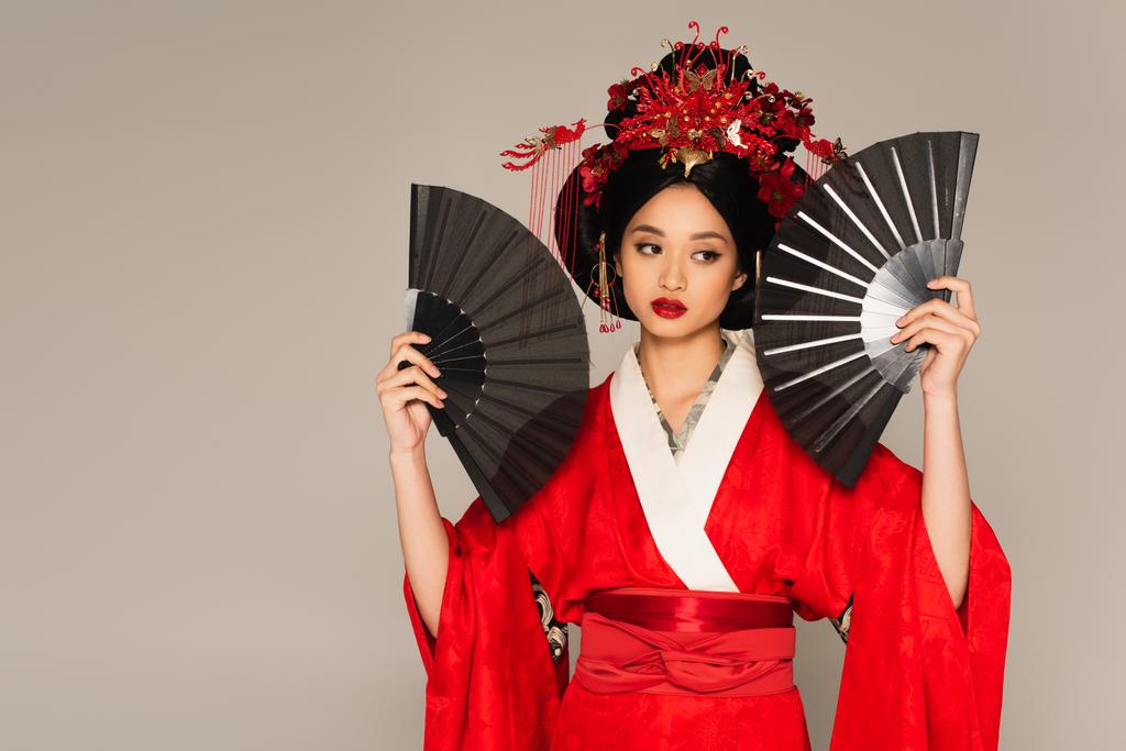 Японская женщина в кимоно позирует с вентиляторами, изолированными на сером  - Фото, изображение
