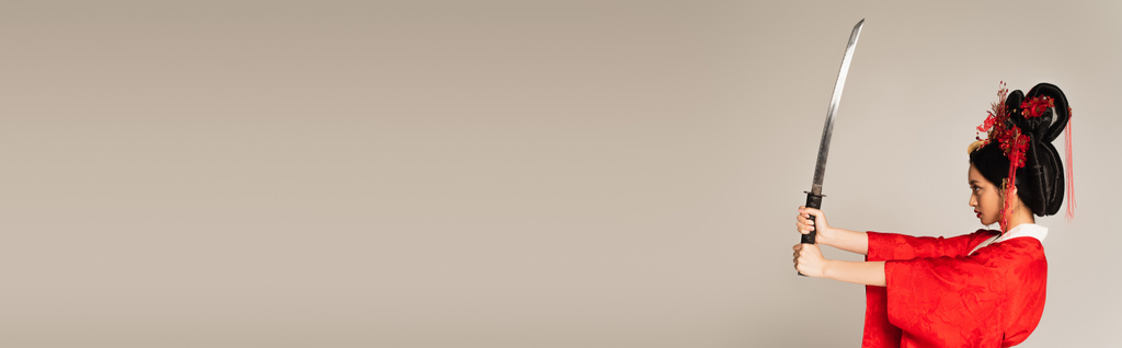 Πλευρική άποψη της Ασιάτισσας με κόκκινο κιμονό κρατώντας το σπαθί απομονωμένο σε γκρι, λάβαρο - Φωτογραφία, εικόνα