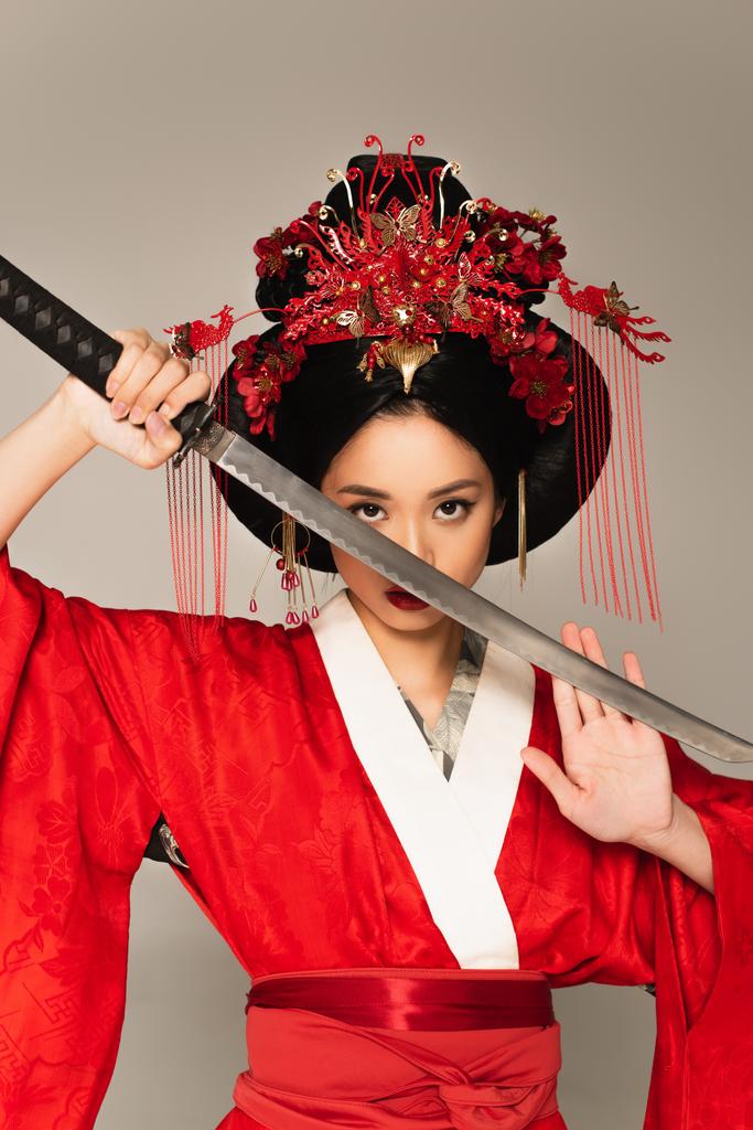 Ασιάτισσα γυναίκα με διακόσμηση στο χτένισμα κρατώντας σπαθί απομονωμένο σε γκρι  - Φωτογραφία, εικόνα