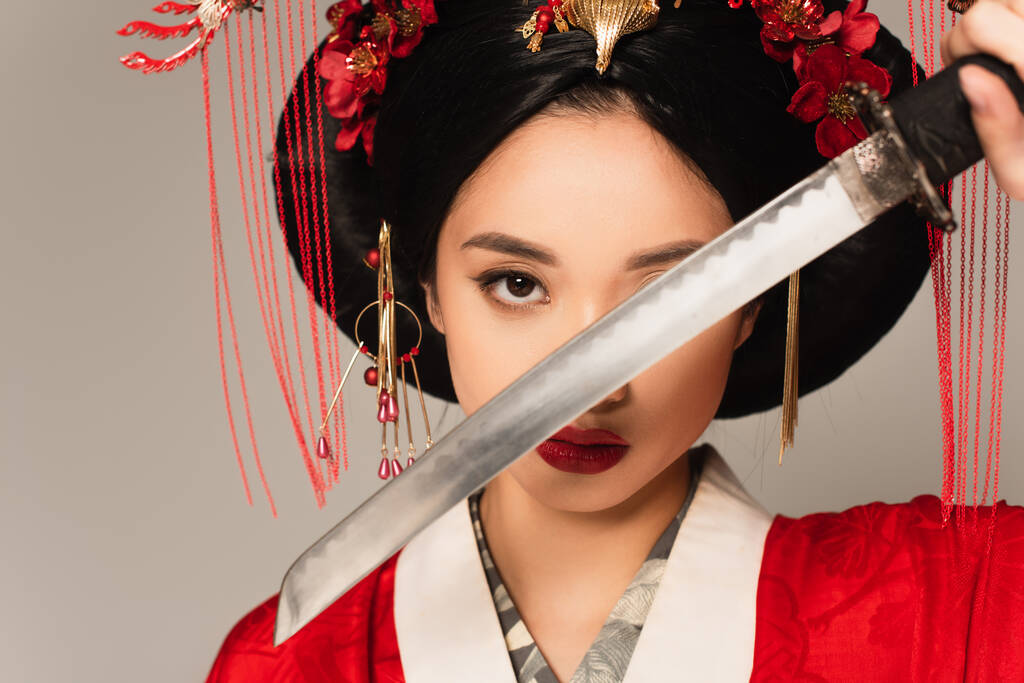 Japanese woman in national costume holding blurred sword near face isolated on grey  - Photo, Image