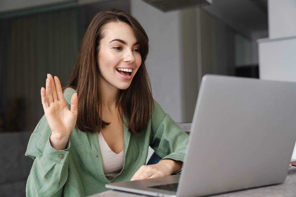 Neşeli kadın evde bilgisayarla video görüşmesi yaparken el sallıyor. - Fotoğraf, Görsel
