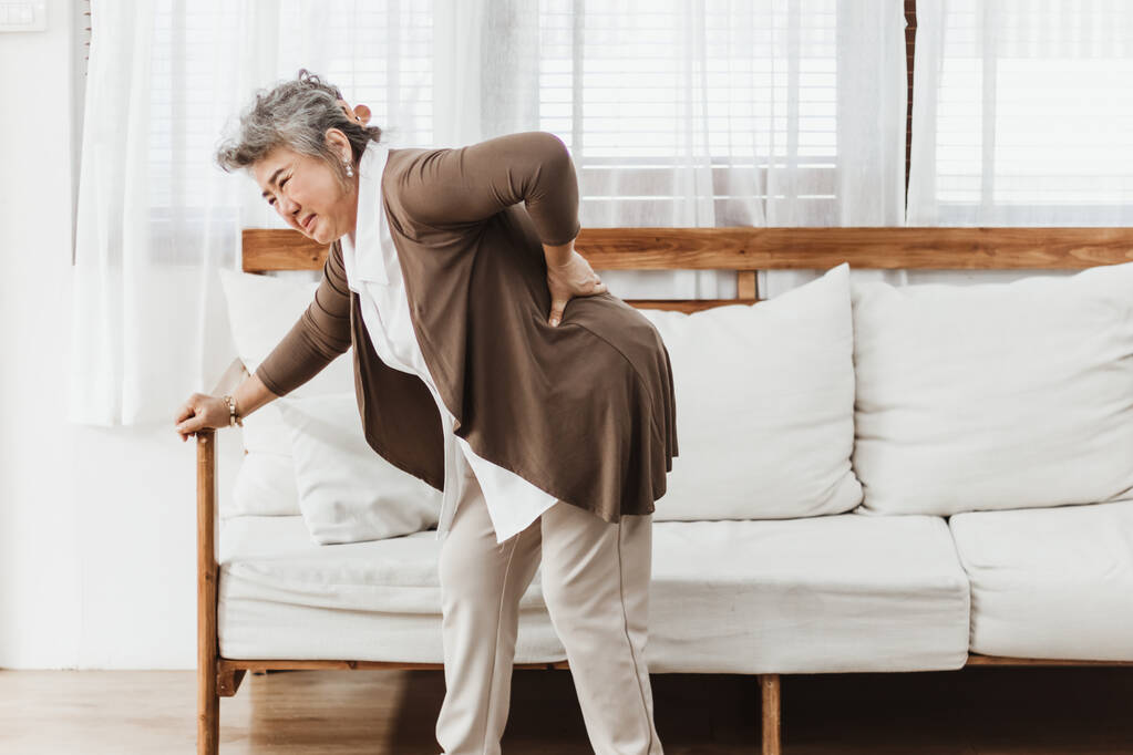 Femme âgée asiatique souffrant de maux de dos, seule à la maison. Femme âgée souffrant d'ostéoporose ou d'une blessure au dos. Assurance-vie pour les personnes âgées avec concept de soins de santé et de traitement - Photo, Image