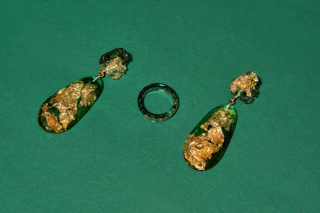 Stijlvolle set van handgemaakte ring en bengelen oorbellen gemaakt van epoxyhars met gouden folie binnen geïsoleerd over groene achtergrond - Foto, afbeelding