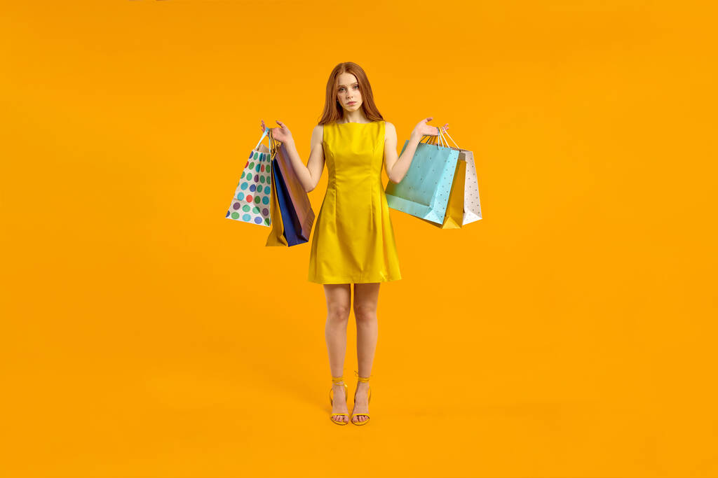 Zklamaná rudovlasá žena v šatech drží nákupní balíčky, rozrušený nákupy - Fotografie, Obrázek