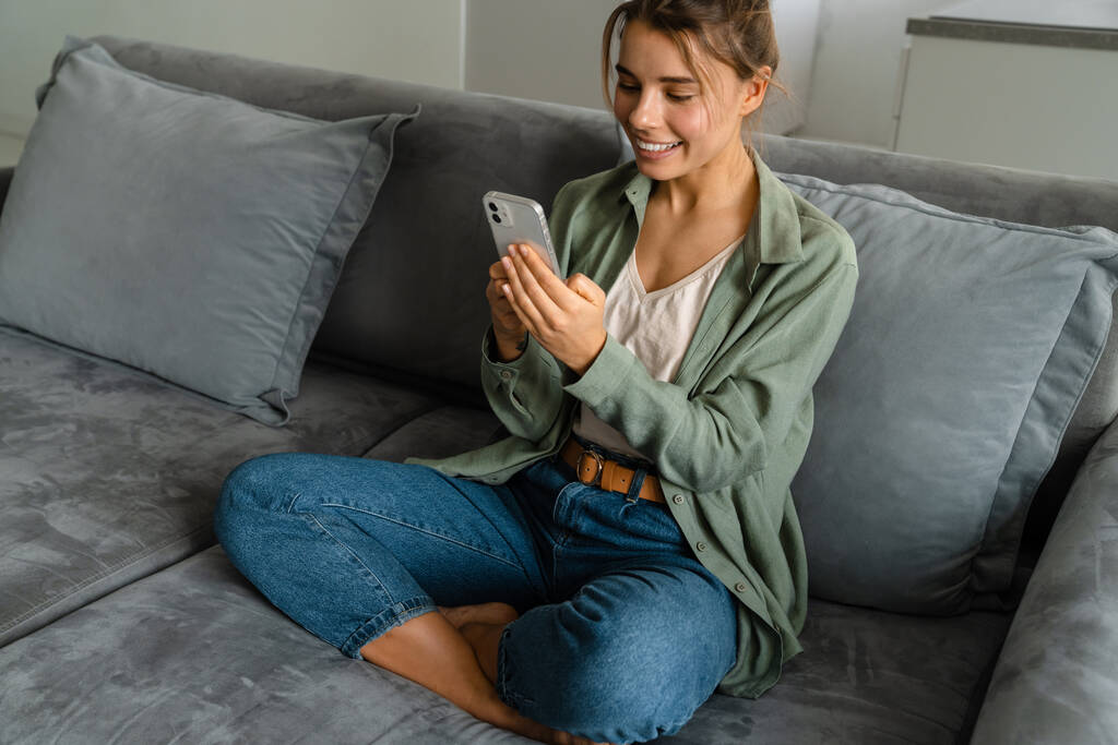 自宅でソファに座っている間、携帯電話を使用して幸せな素敵な女性 - 写真・画像