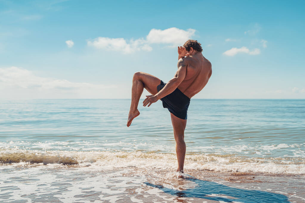 Un muay thai o kickboxer entrenando con boxeo de sombras al aire libre en la orilla del mar - Foto, Imagen