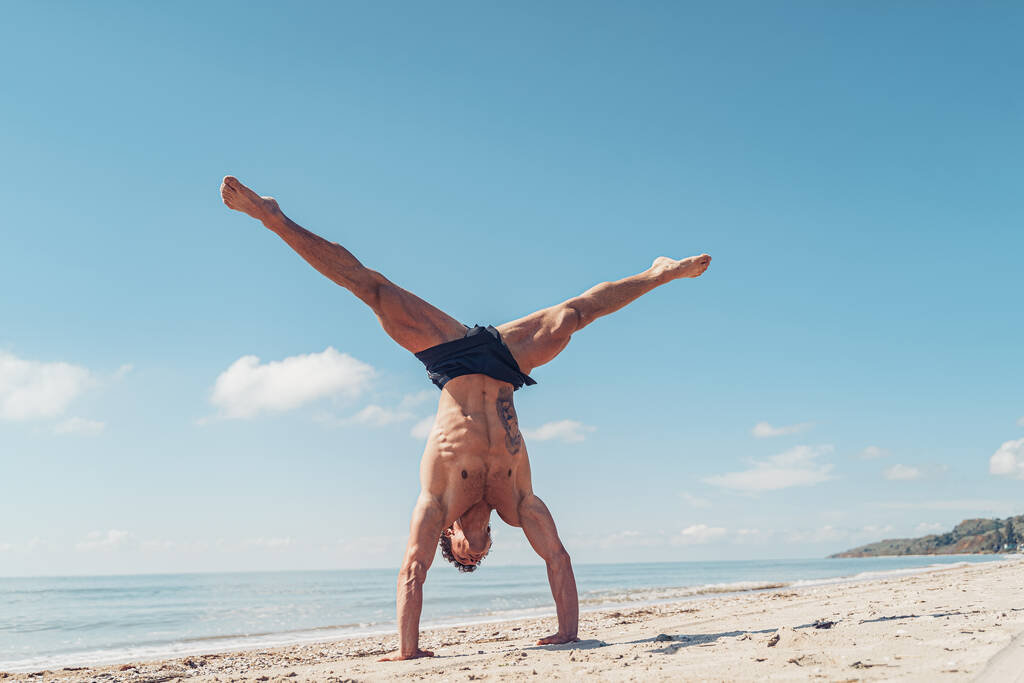 Muscular culturista fitness hombre con un torso desnudo se levanta en el brazo en la playa - Foto, Imagen