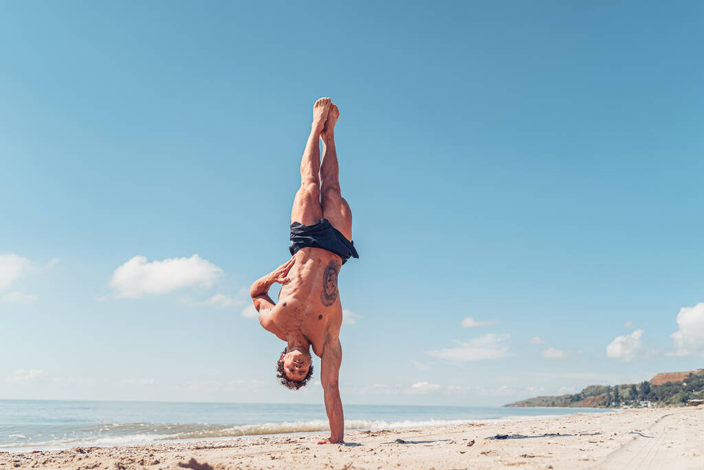 М'язистий культурист фітнес-людина з голим торсом стоїть на одній руці на пляжі
 - Фото, зображення