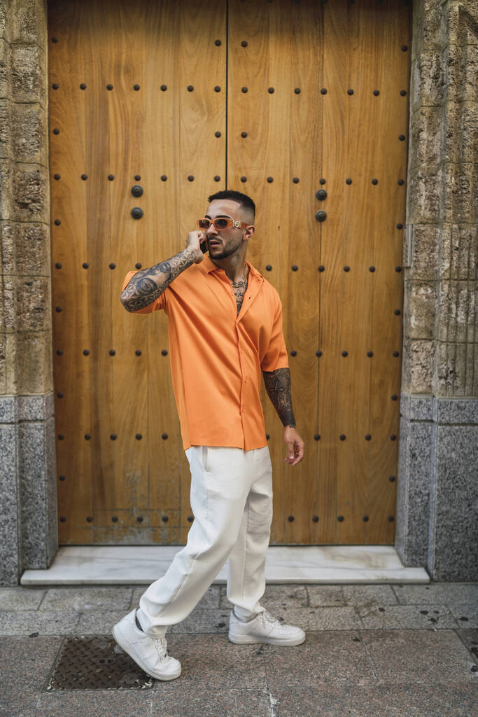 Pystysuora kuva miehestä, joka käyttää rentoja vaatteita ja puhelinta vanhassa rakennuksessa Espanjassa. - Valokuva, kuva