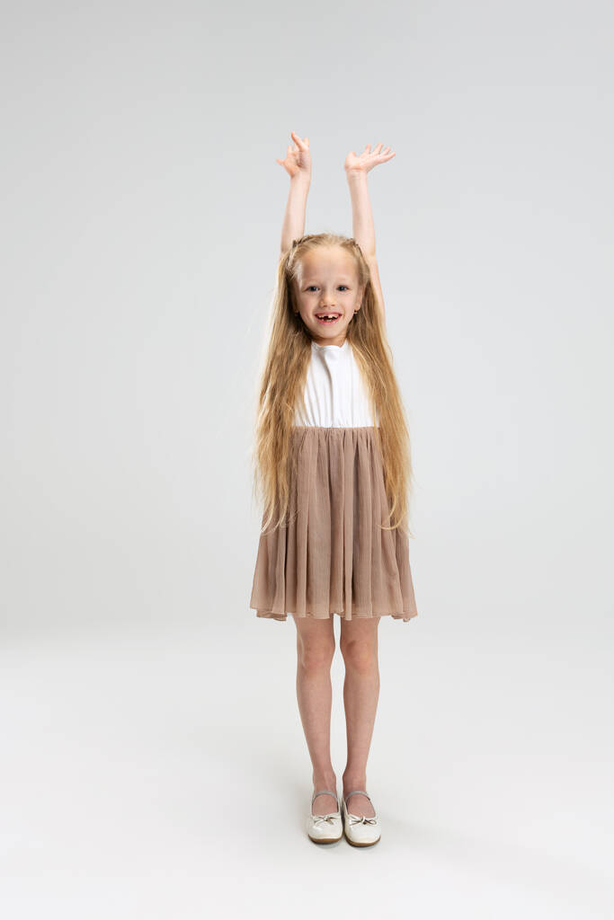 Красива маленька дівчинка в сучасному стильному платті позує ізольовано на білому фоні студії. Концепція щасливого дитинства
. - Фото, зображення