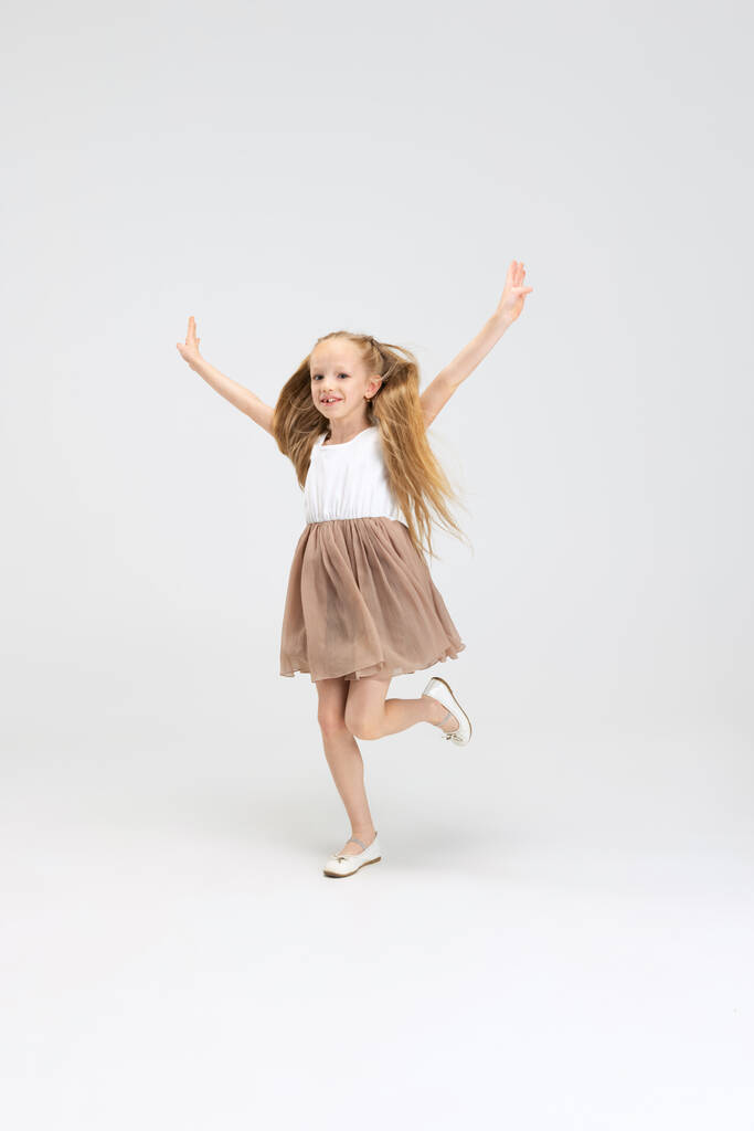 Piękna dziewczynka w nowoczesnej stylowej sukience pozowanie izolowane na białym tle studio. Szczęśliwego dzieciństwa. - Zdjęcie, obraz