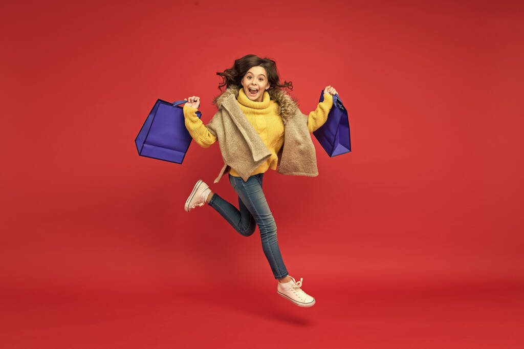 χαρούμενο παιδί που τρέχει με πακέτα αγορών μετά από μια επιτυχημένη μέρα στο εμπορικό κέντρο, εποχιακές εκπτώσεις - Φωτογραφία, εικόνα