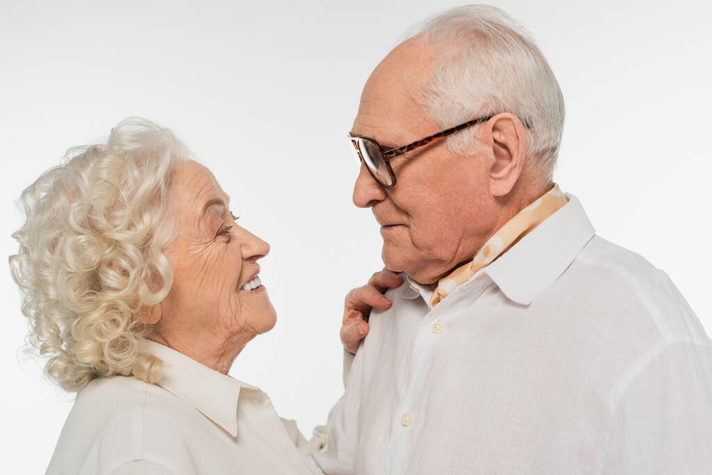 Älteres Paar in legerer Kleidung umarmt sich und sieht sich vereinzelt auf weißem Grund an - Foto, Bild