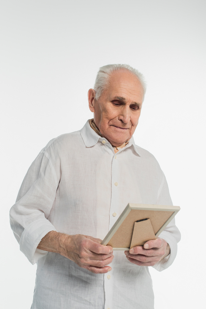 αναστατωμένος ηλικιωμένος άνδρας με πουκάμισο κρατώντας κορνίζα σε χέρια που απομονώνονται σε λευκό - Φωτογραφία, εικόνα
