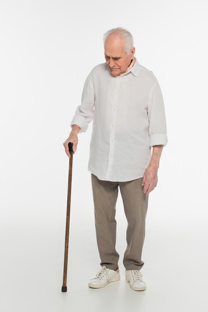 Aufgebrachter älterer Mann in Freizeitkleidung steht mit Spazierstock auf weißem Grund - Foto, Bild