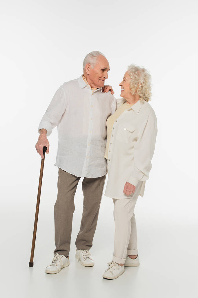 Lächelnde ältere Frau blickt Mann mit Gehstock auf weißem Grund an - Foto, Bild