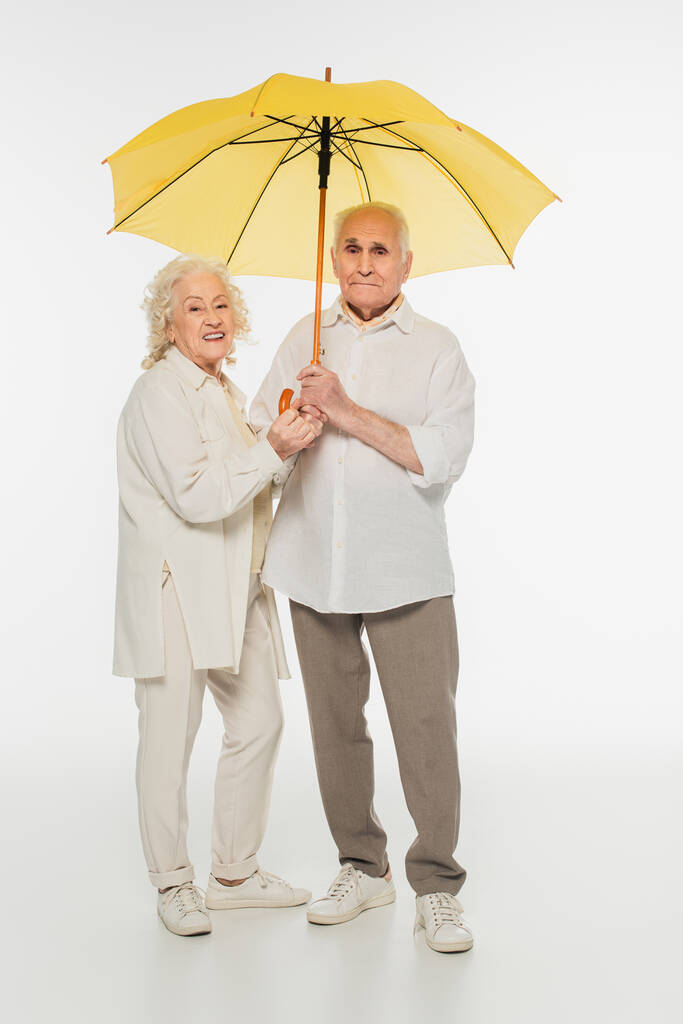 heureux couple âgé debout avec parapluie jaune sur blanc - Photo, image