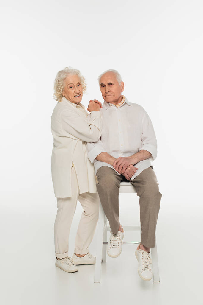 χαμογελαστή ηλικιωμένη γυναίκα που αγκαλιάζει τον άντρα της κάθεται στα λευκά - Φωτογραφία, εικόνα
