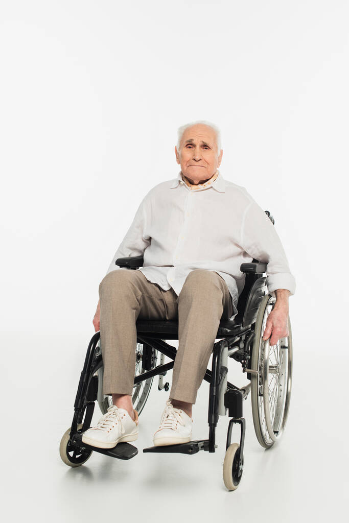 esausto uomo anziano in abiti casual seduto in sedia a rotelle su bianco - Foto, immagini