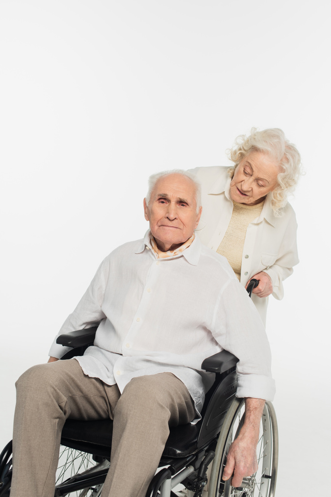 Kocasıyla beyaz tekerlekli sandalyede yuvarlanan yaşlı kadın. - Fotoğraf, Görsel