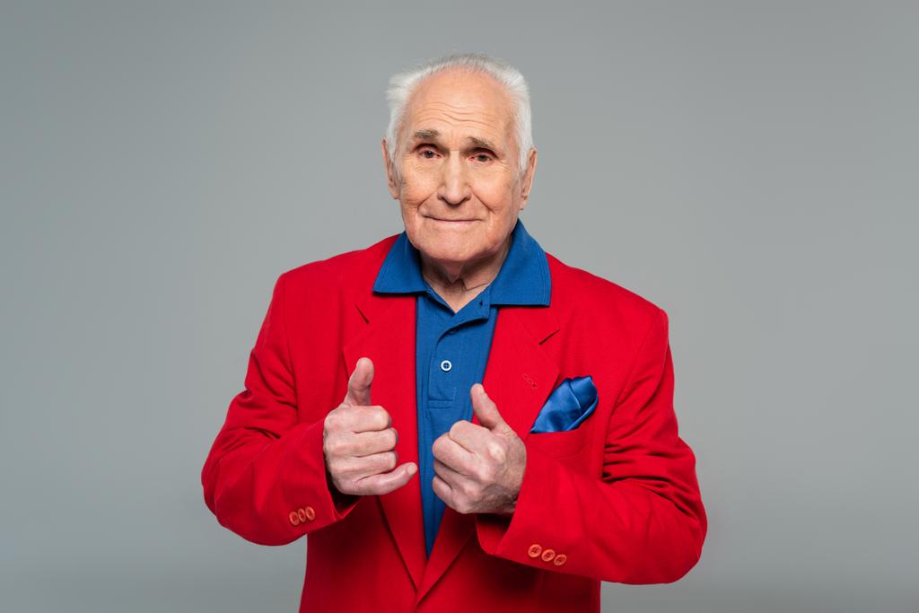 senior man in rode blazer staande duimen omhoog gebaren geïsoleerd op grijs - Foto, afbeelding