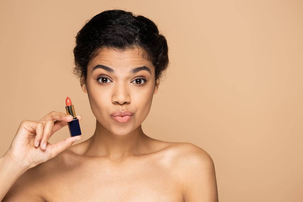 african american woman pouting lips and holding lipstick isolated on beige  - Photo, Image