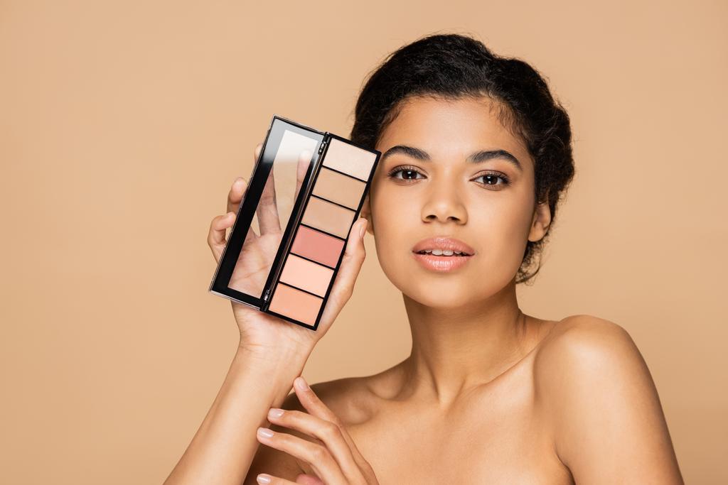 jovem afro-americana com ombros nus segurando blush paleta isolada no bege  - Foto, Imagem
