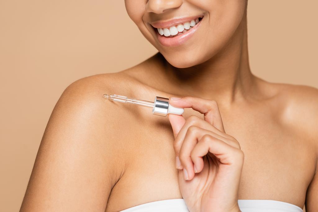 cropped view of happy african american woman with bare shoulders applying serum on bare shoulder isolated on beige  - Photo, Image