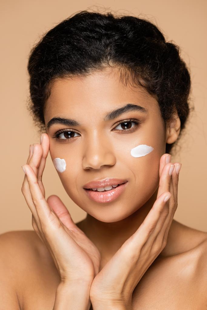 giovane donna afroamericana con crema viso sulle guance isolata sul beige  - Foto, immagini