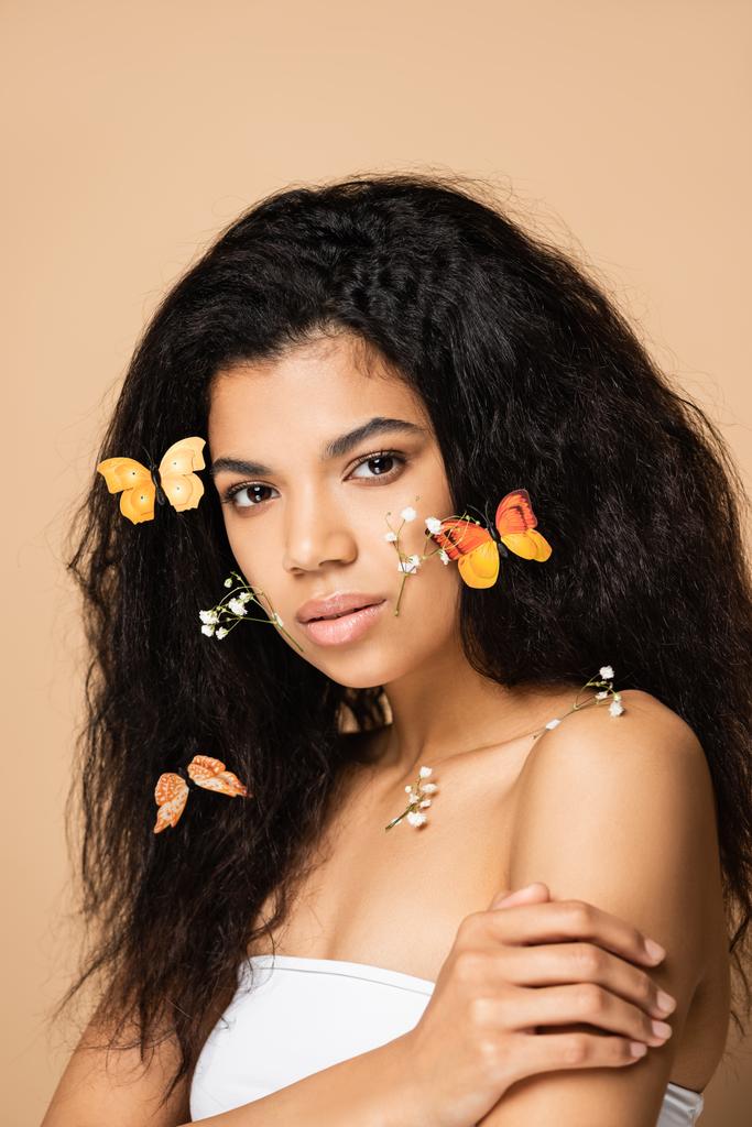 junge afrikanisch-amerikanische Frau mit kleinen Blüten und orangefarbenen Schmetterlingen auf den Haaren isoliert auf beige - Foto, Bild