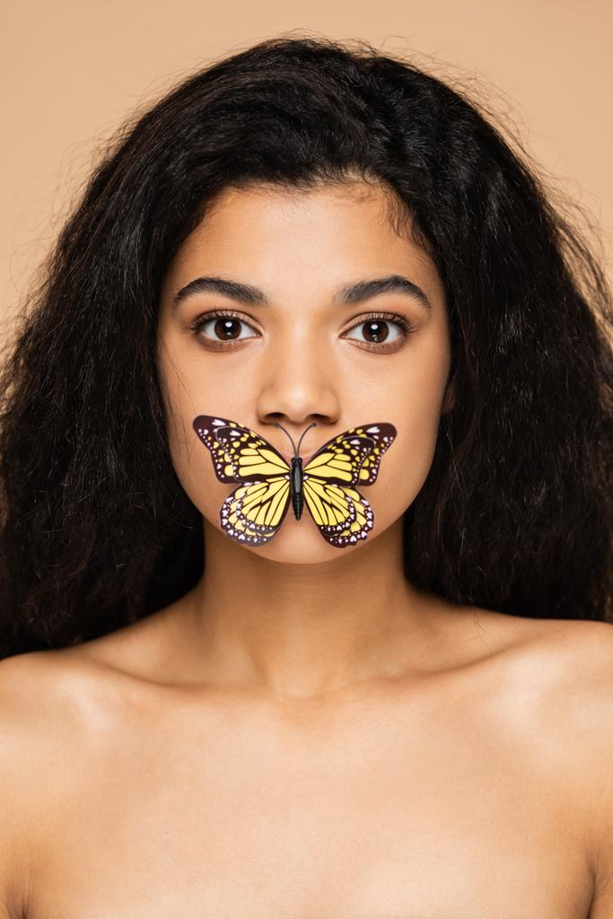 vrij Afrikaans amerikaans jong vrouw met vlinder op lippen geïsoleerd op beige  - Foto, afbeelding