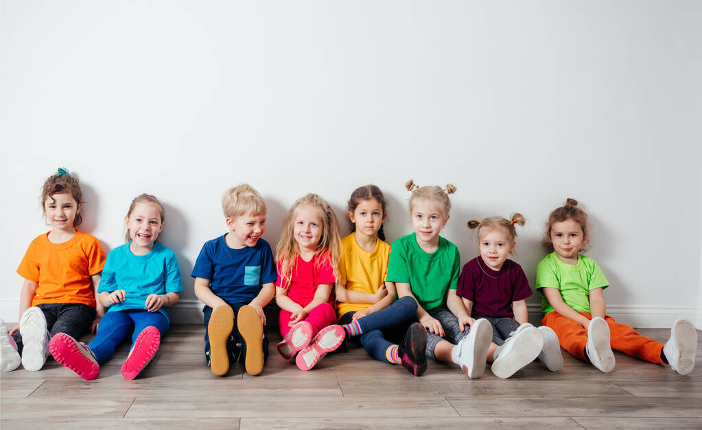 Fröhliche Kinder sitzen auf einem Fußboden neben der Wand - Foto, Bild