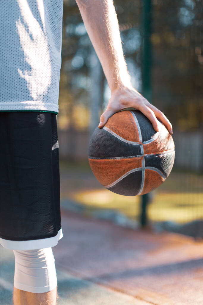 Рука тримає баскетбольний м'яч, крупним планом чоловічий професійний баскетболіст на відкритому повітрі влітку
 - Фото, зображення