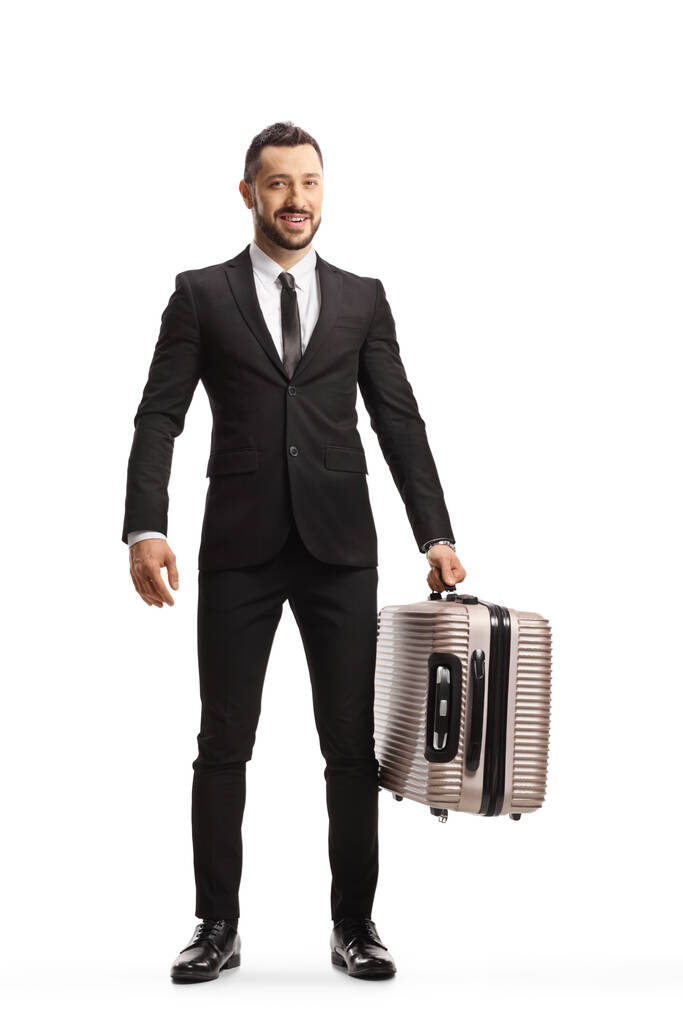 Teljes hosszúságú portré egy öltönyös és nyakkendős férfiról, aki bőröndöt cipel, és fehér alapon elszigetelt kamerát néz. - Fotó, kép