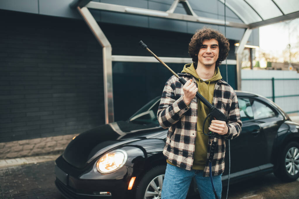 Usmívající se řidič drží tlakové myčky aut v blízkosti auto na samoobslužné mytí - Fotografie, Obrázek