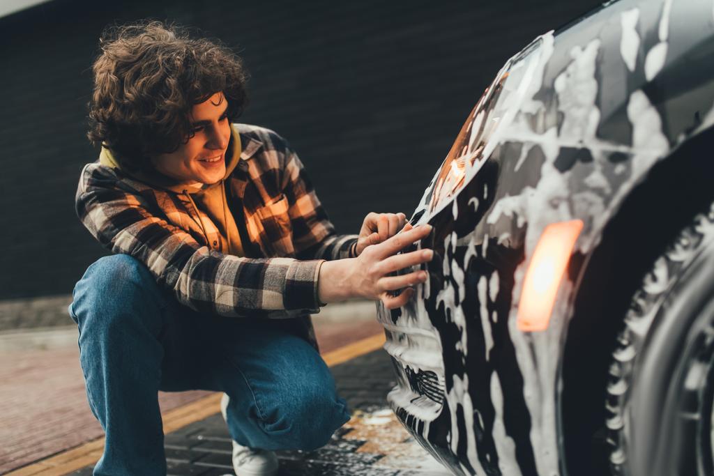 Uśmiechnięty mężczyzna patrząc na samochód w detergencie na samoobsługowej myjni  - Zdjęcie, obraz