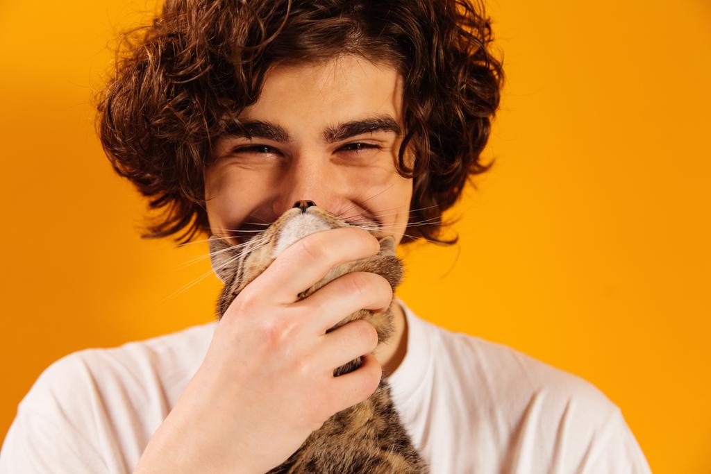 Cheerful man holding cat and looking at camera isolated on orange  - Photo, Image