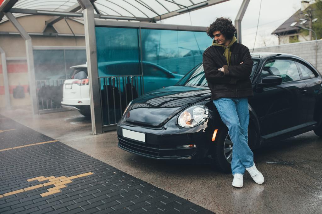 Mladý muž se zkříženými pažemi při pohledu na čisté auto na samoobslužné mytí - Fotografie, Obrázek