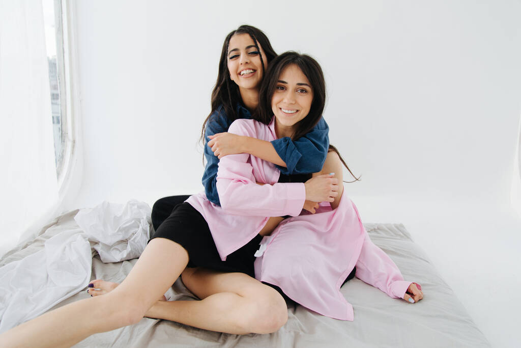 ζευγάρι των νέων και χαρούμενων Αρμένιων γυναικών κοιτάζοντας κάμερα, ενώ αγκαλιάζει στην κρεβατοκάμαρα - Φωτογραφία, εικόνα
