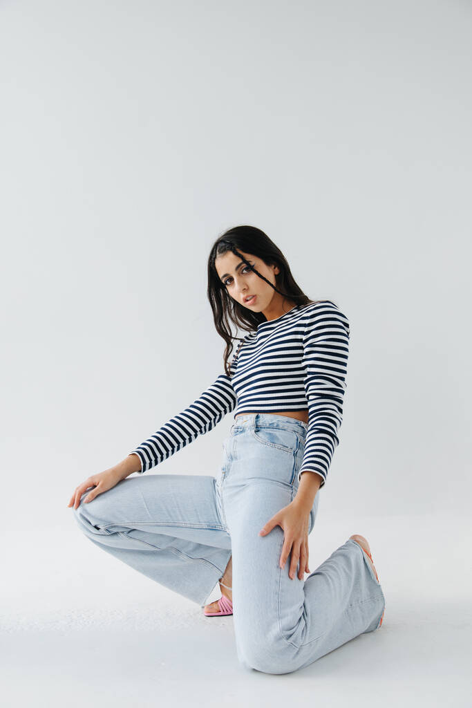 pretty armenian woman in jeans and striped pullover posing on white background - Photo, Image